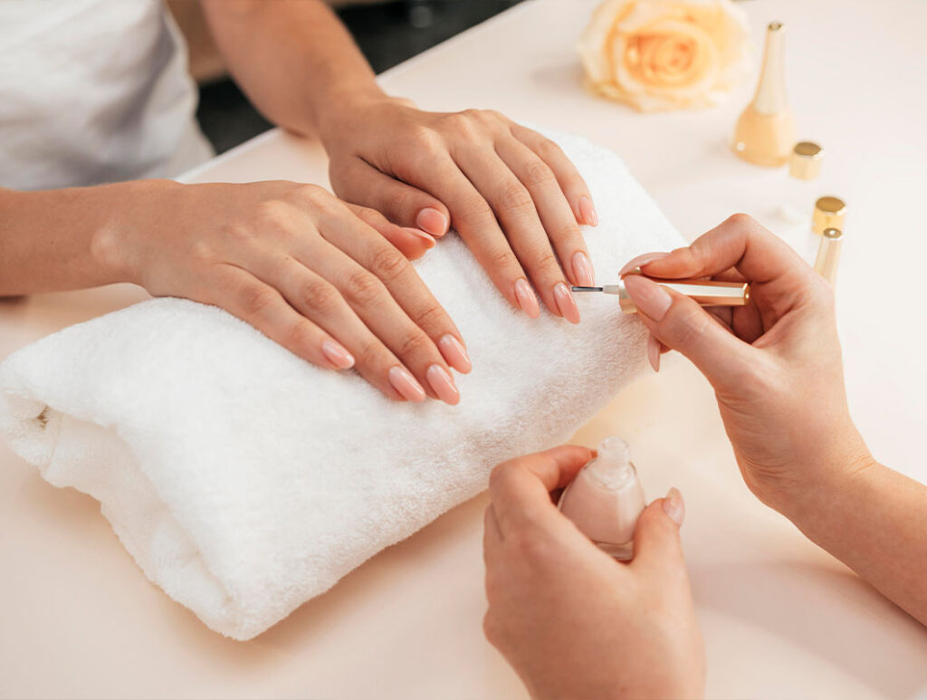Professional nail artist applying a glossy nude gel polish to a client's almond-shaped nails in a clean, high-end studio setting