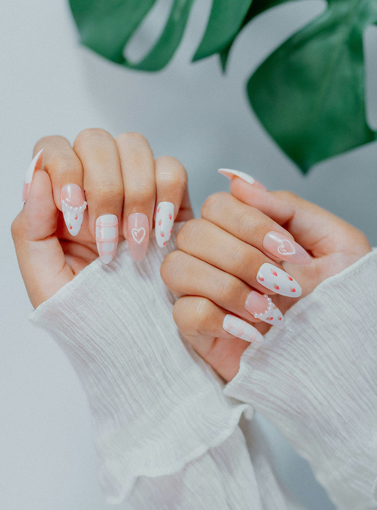 Close-up of elegant almond-shaped nail art featuring hand-painted white hearts, dainty strawberry patterns, and pearl accents for Butterfly Nail Art Studio