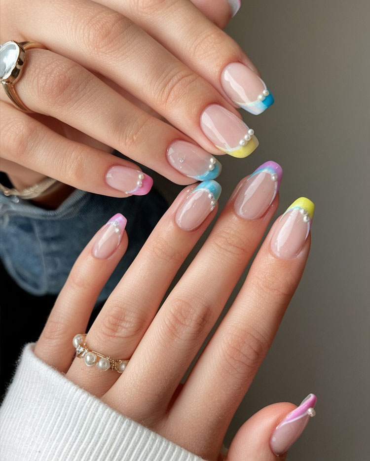 Close-up of modern French nail art featuring colorful pastel tips with elegant pearl accents on almond-shaped nails