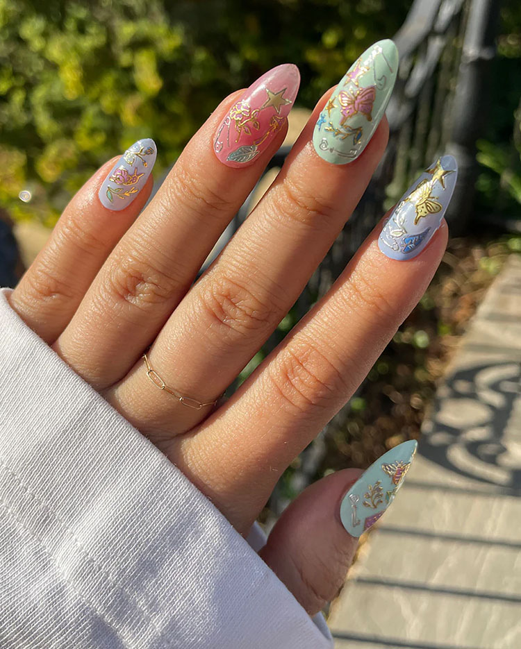 Artistic sticker nail art on pastel almond nails featuring gold butterfly and floral decals for a whimsical, creative look